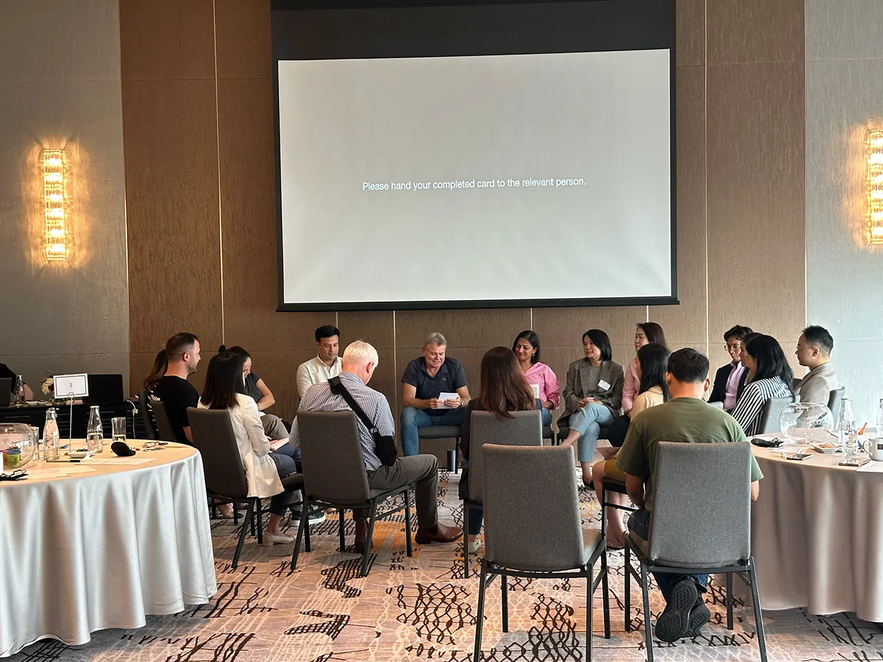 A leadership team seated in a circle around a facilitator, handing in completed cards during an exercise